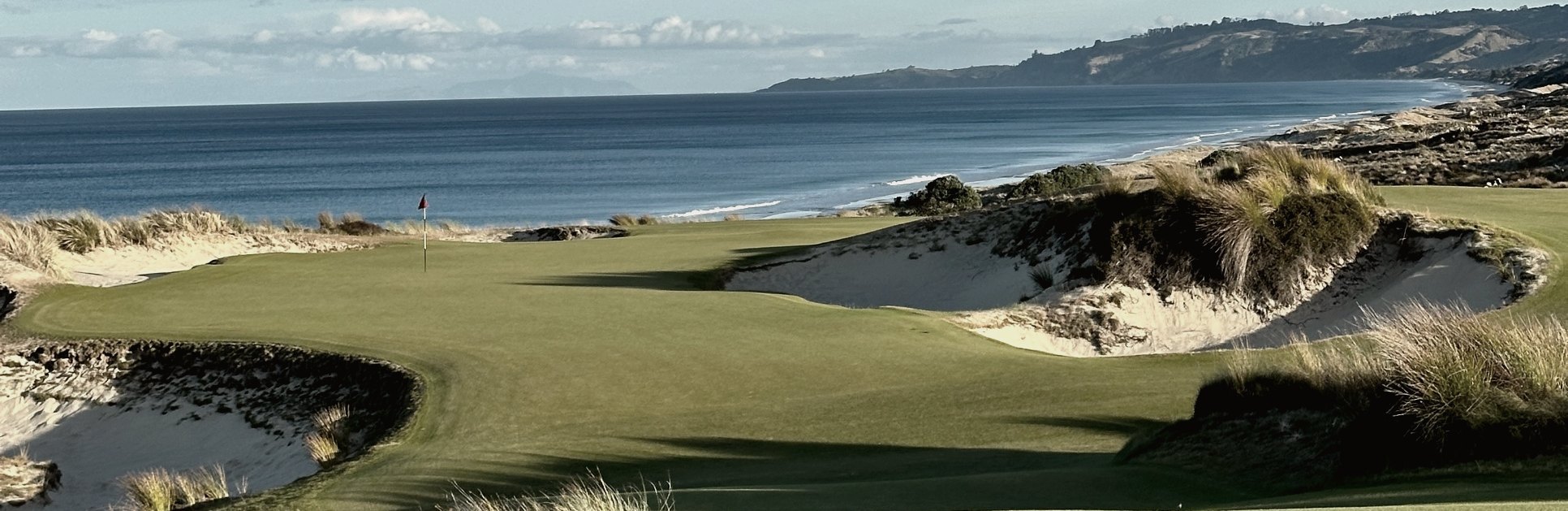 Green framed by sand dunes above the ocean at Te Arai Links
